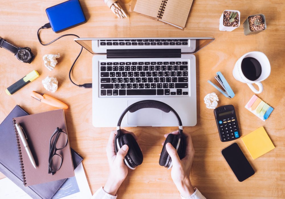 Top view of Male hands holding headphones, Laptop with office supplies on wooden desk.